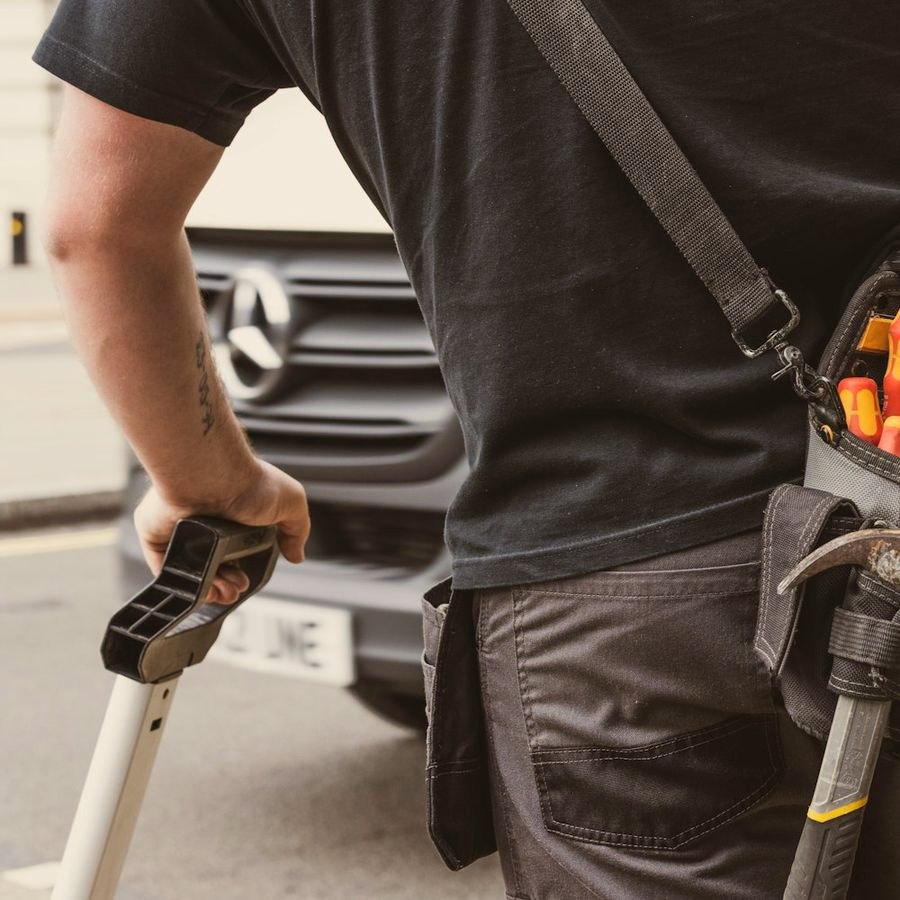 A tradesperson with a tool belt beside a vehicle